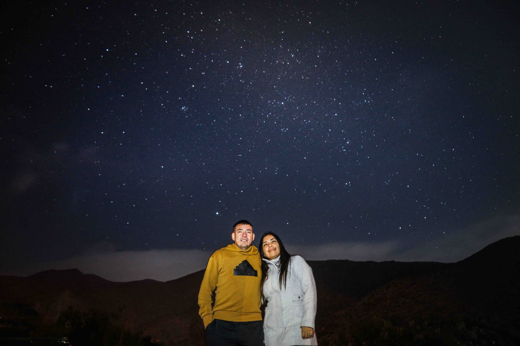 Una pareja abrazada bajo el cielo estrellado del Molle, con los cerros recortados detrás.
